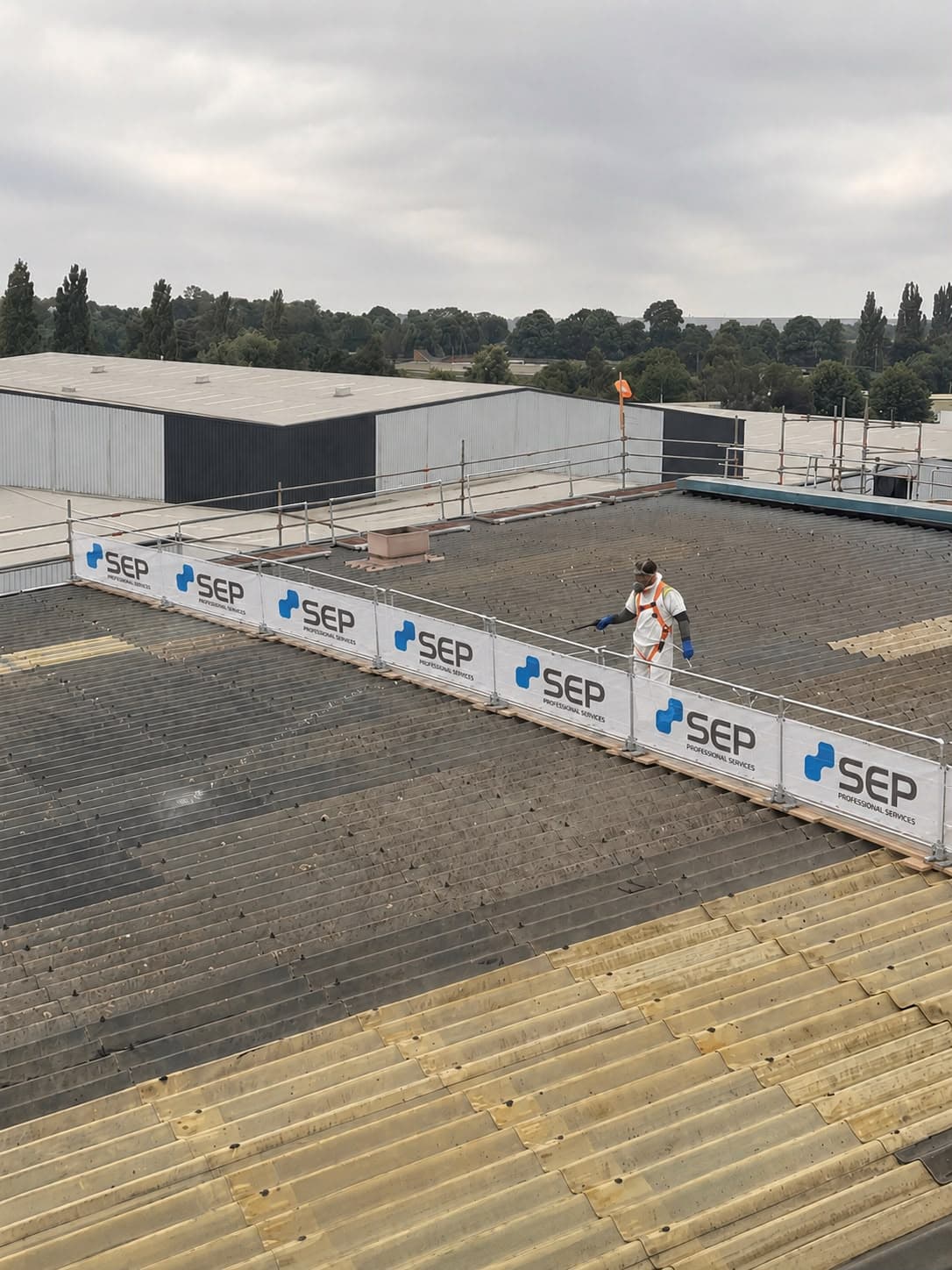 SEP operative working at height behind SEP-branded roof edge protection on a live industrial site